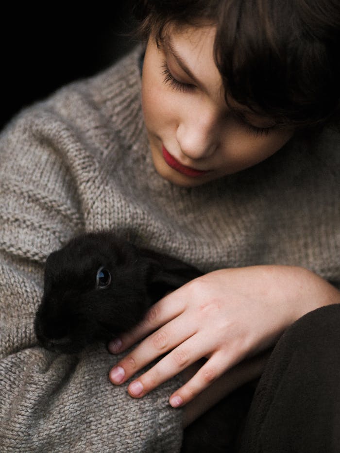 Child in wool sweater gently hugging a black rabbit, evoking warmth and tenderness.